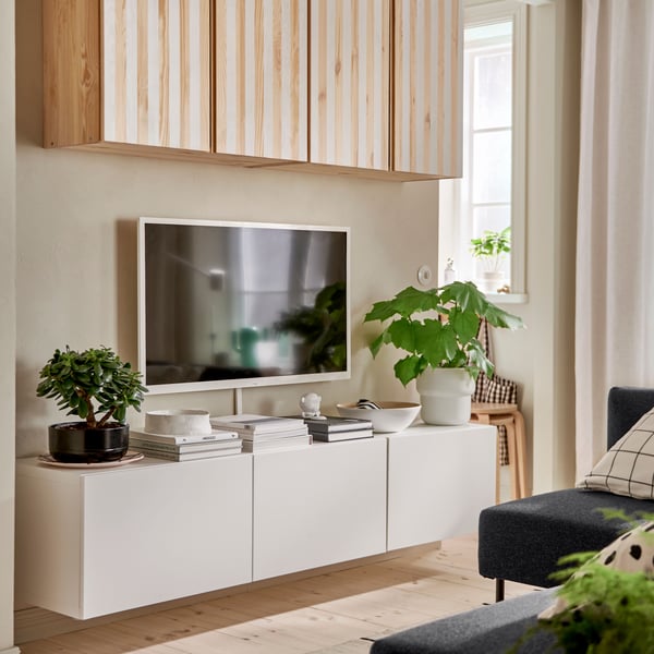 A white BESTÅ TV bench with doors is mounted on a wall underneath a wall-mounted TV and IVAR cabinets painted with stripes.