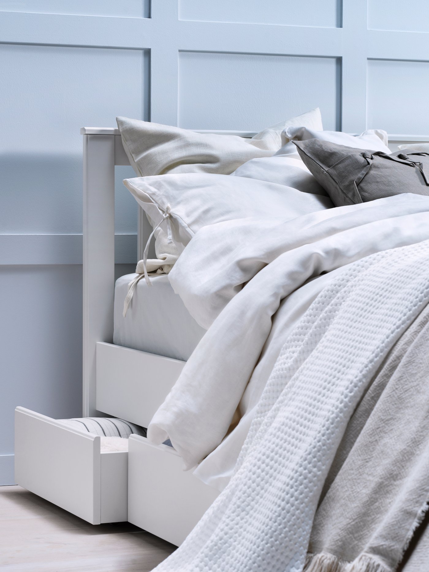 A person in pyjamas lying in a birch-frame bed with white bedlinen and a beige ODDRUN throw, next to a white bedside table.