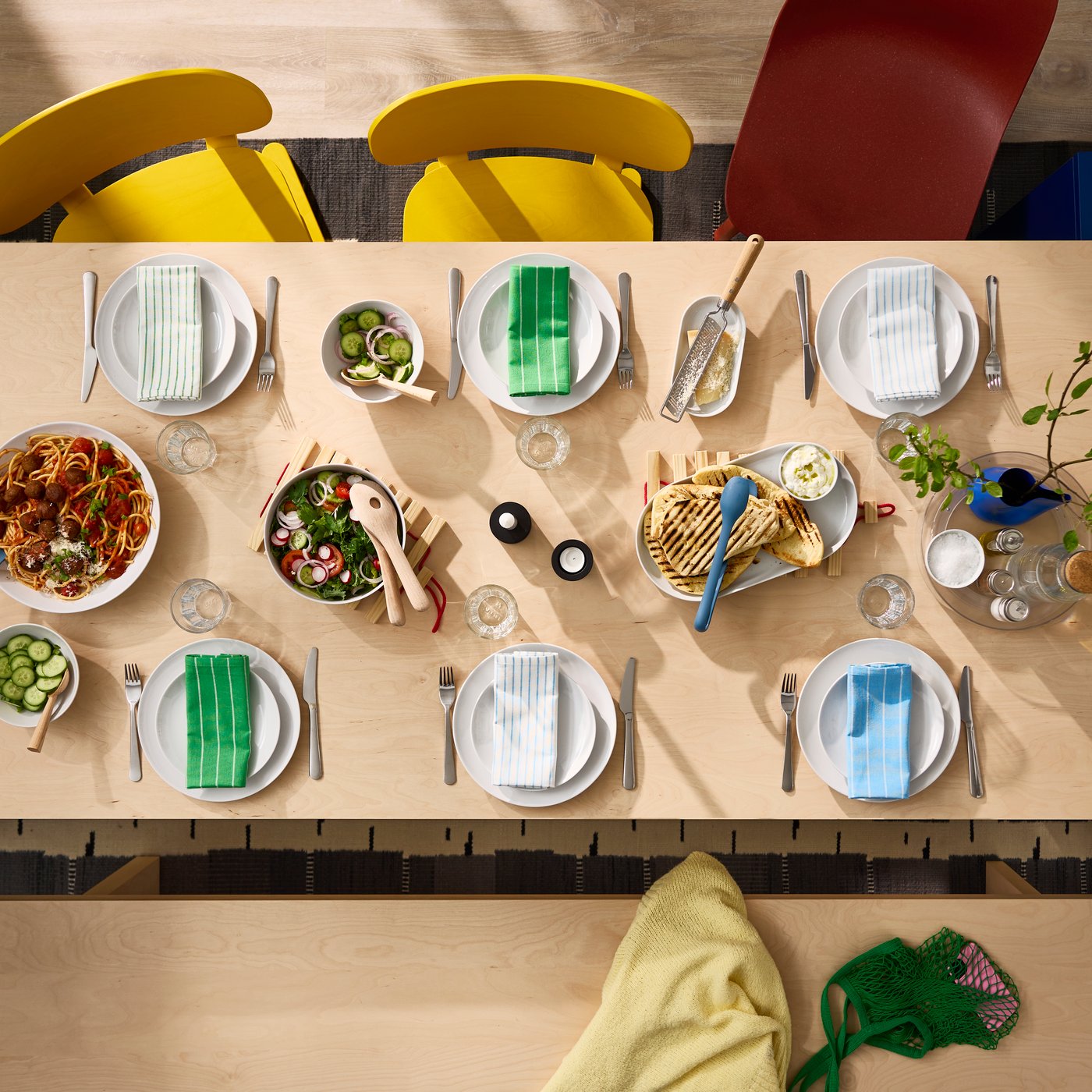 Blick von oben auf einen gedeckten BERGSHYTTAN Esstisch in Birkenfurnier. Außerdem zwei gelbe Stühle und ein roter ODGER Sesel.