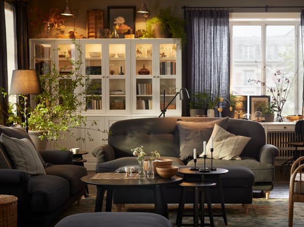 A farmhouse-style living room with plenty of framed works of art and books, two ESSEBODA sofas and some KRAGSTA tables.