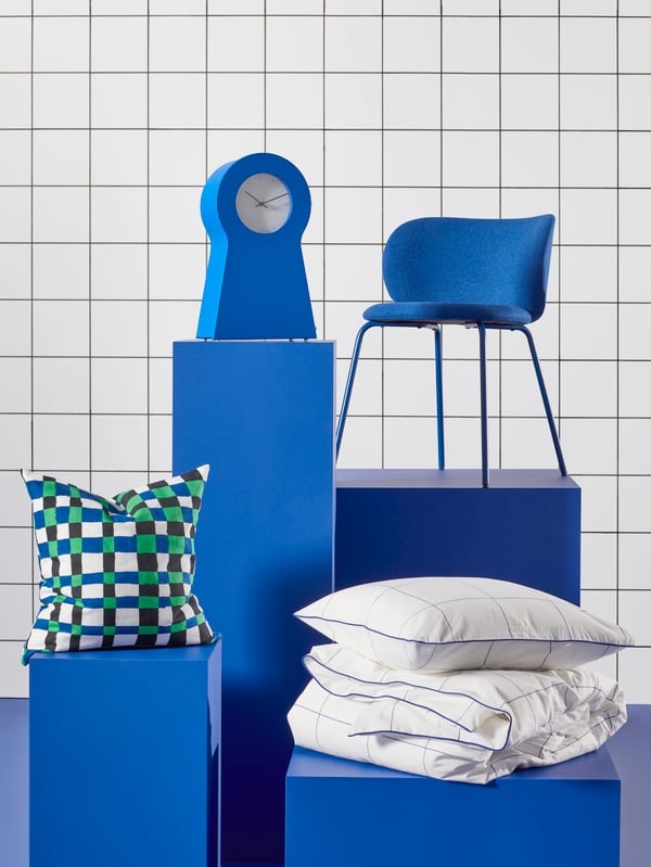 Cuatro productos en podios. Fundas nórdica/de cojín BREDVECKLARE, un cojín PLATTLUMMER, un reloj IKEA PS 1995 y la silla KRYLBO azul.