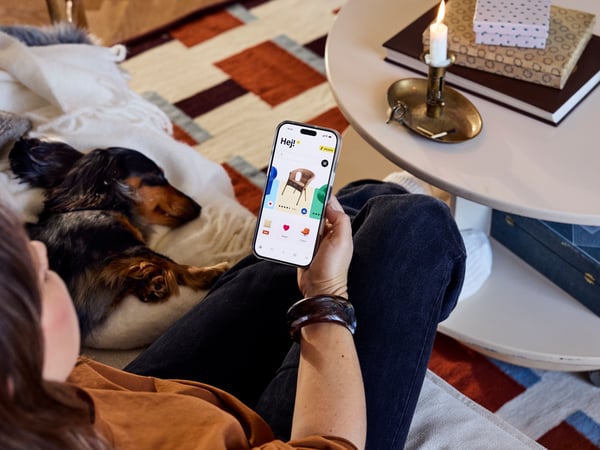 Kobieta trzymająca telefon z włączoną aplikacją IKEA ogladająca meble, obok leży jamnik.