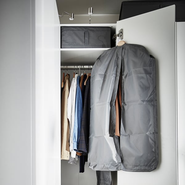 A dark gray SKUBB garment bag hangs on the open door of a wardrobe