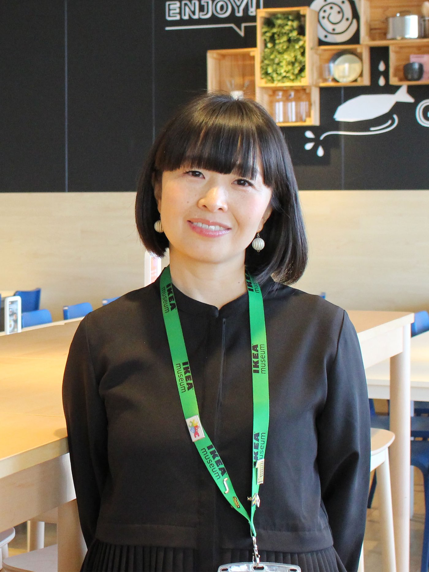 イケアレストランのテーブルエリアで、ネームプレートと緑のストラップを付けたコワーカーが立っている