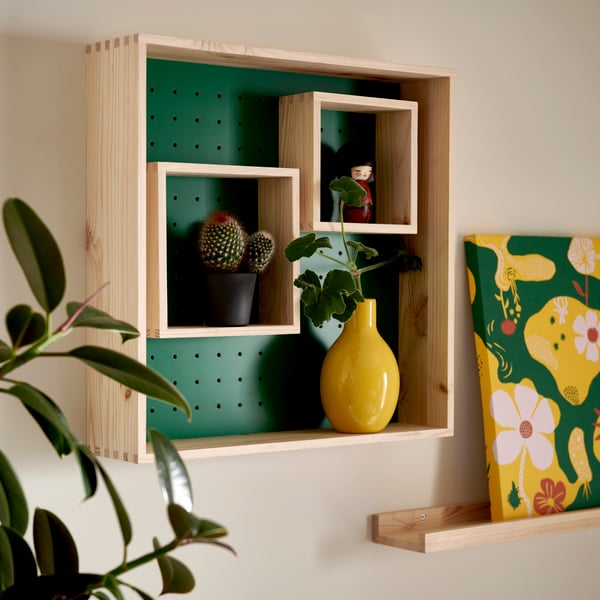 A green SKOGSMOSAIK display shelf showcases cacti and a vibrant yellow vase, set against a sleek wall.