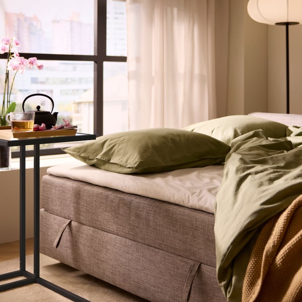 A light grey FRIHETEN corner sofa-bed with storage and a small side table holding tea and snacks.