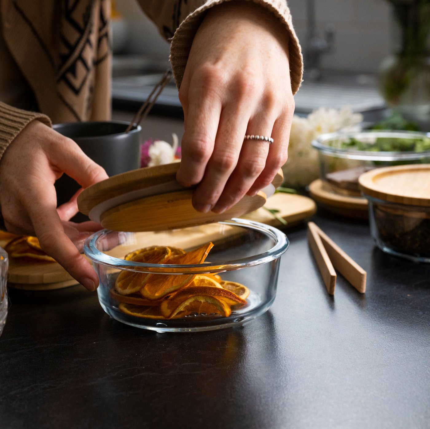 Dve roki odpirata pokrov IKEA 365+ posode za živila, v kateri so rezine pomaranče.