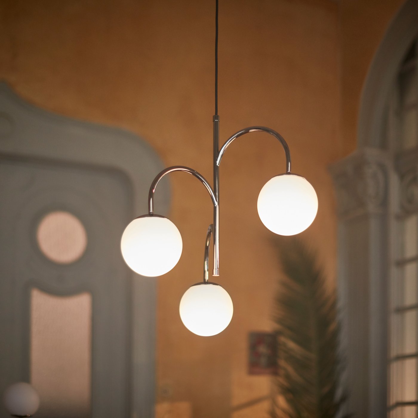 A 3-armed SIMRISHAMN pendant lamp hangs from the ceiling in a room with beige walls near an elaborate door.