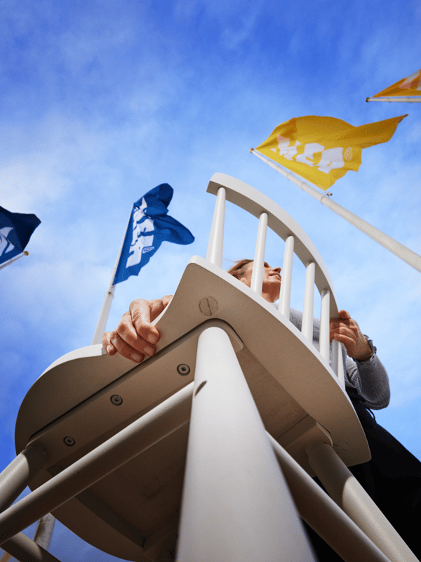 A person is carrying a chair outdoors, surrounded by IKEA flags.