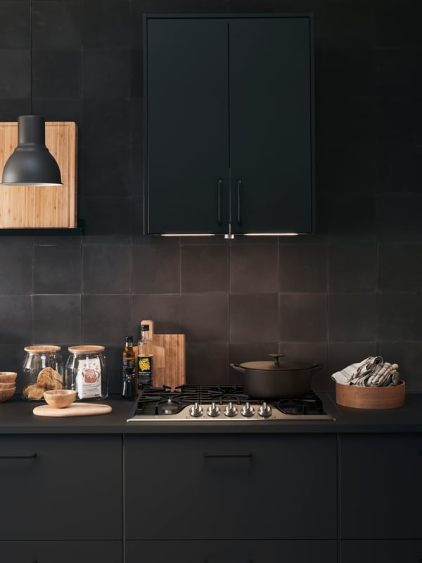 A kitchen cooking area with SEKTION cabinets and a black HEKTAR lamp.