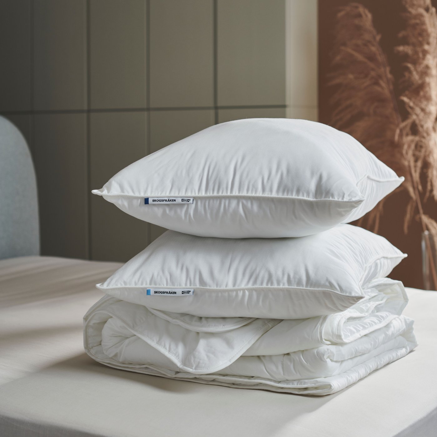 Two high SKOGSFRÄKEN pillows without pillowcases are stacked with a white duvet on a bed, in a modern-style  bedroom.