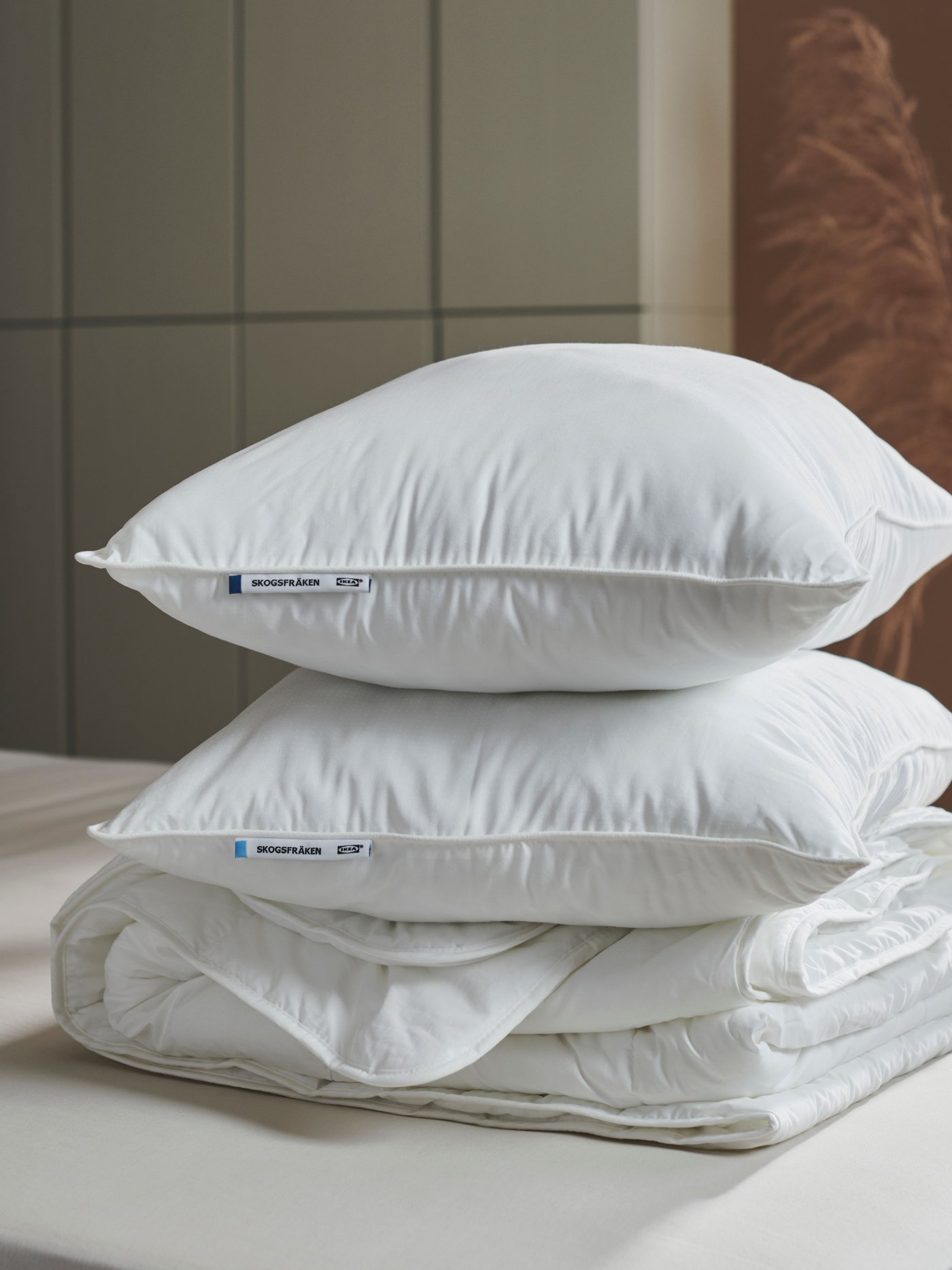 Two high SKOGSFRÄKEN pillows without pillowcases are stacked with a white duvet on a bed, in a modern-style bedroom.