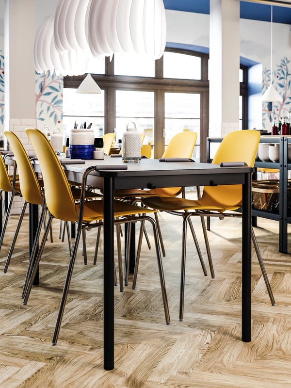 Des chaises jaune foncé avec des accoudoirs suspendues sur une table anthracite, des planchers en bois et des suspensions blanches.