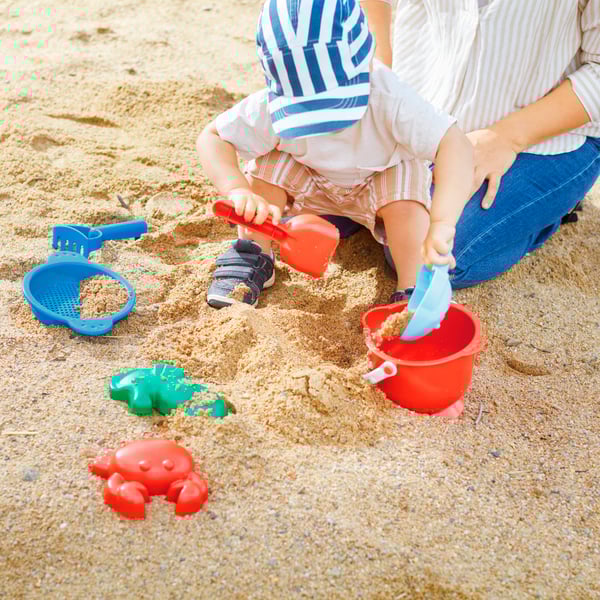 A kid and an adult are playing with a multicolour SANDIG 7-piece sand play set on the beach.