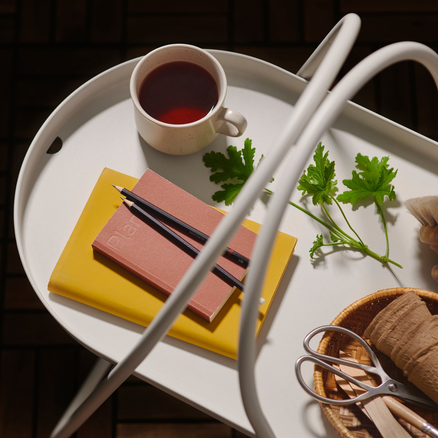 A close-up of a white MÅBÄRSSKÄR coffee table with a cup of tea and pens resting on a notebook, alongside herbs and scissors.