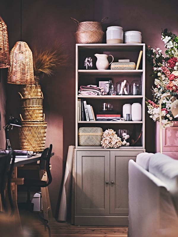 A grey HAVSTA storage combination is filled with decorative items, books, rattan baskets, vases and dried flowers.
