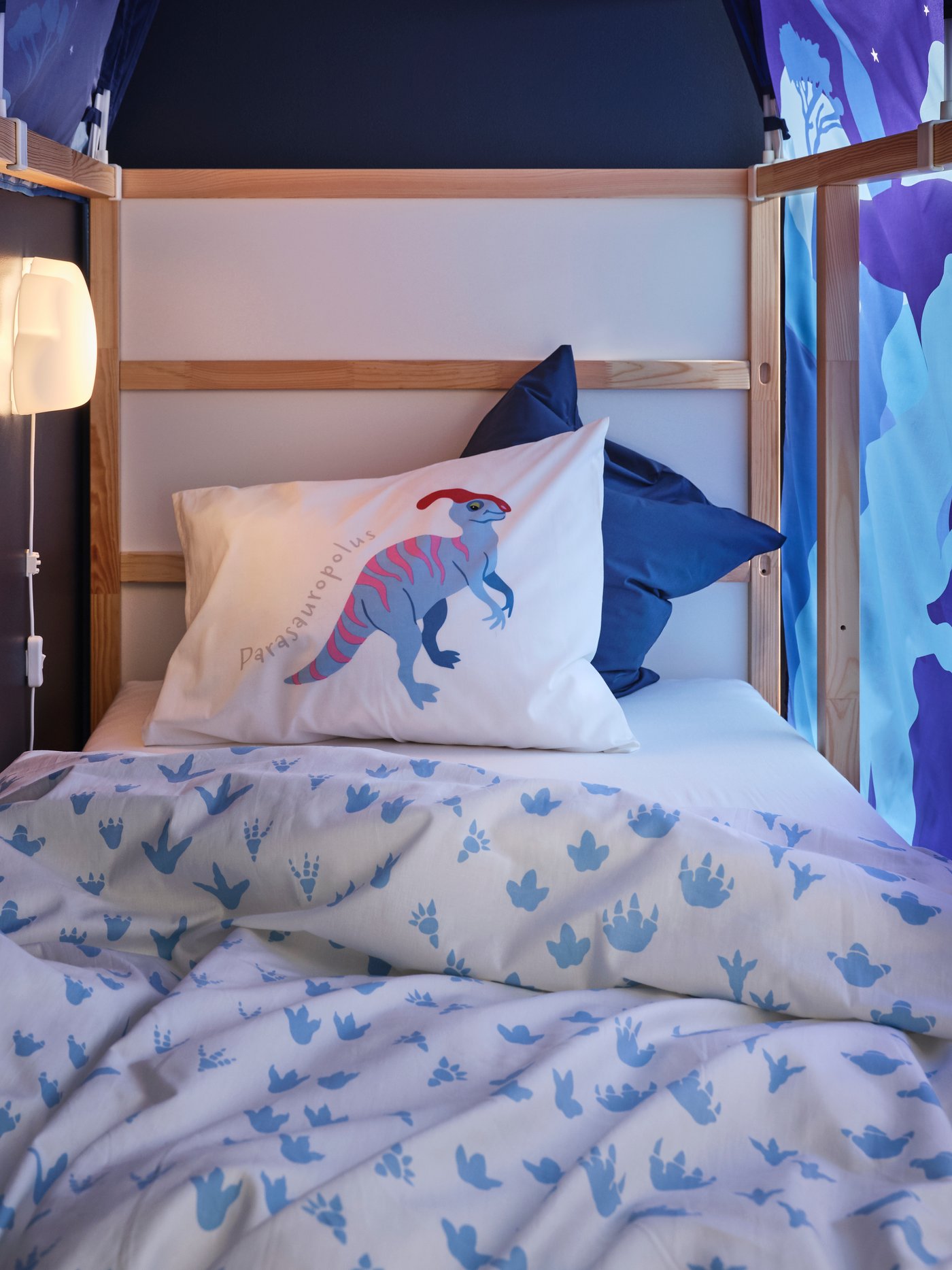 Dormitorio con una funda nórdica y una funda de almohada en color blanco con un estampado de dinosaurios en una cama reversible de color beige.