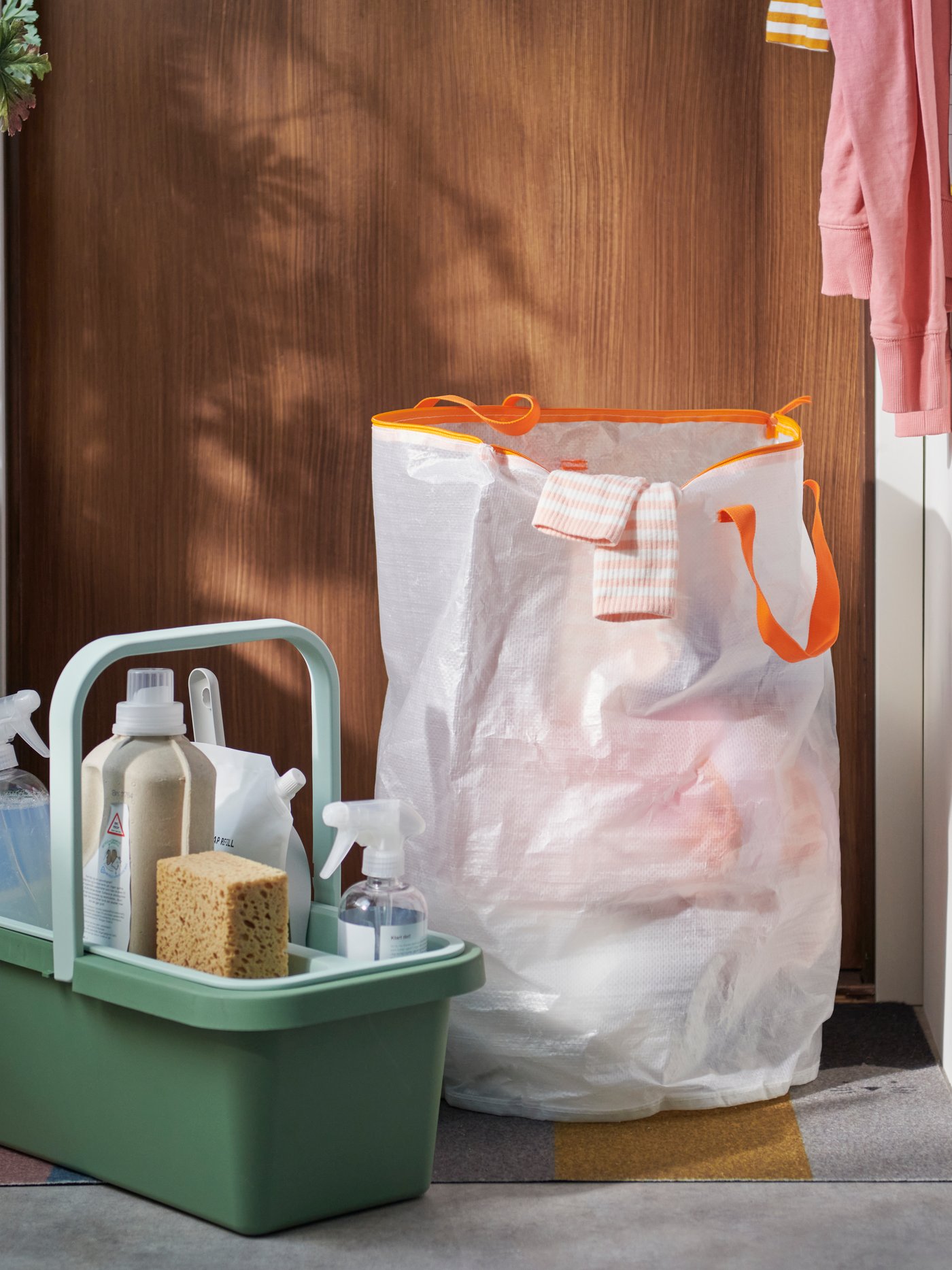 A hallway with a green PEPPRIG cleaning bucket and caddy beside a large white PÄRKLA laundry bag filled with clothes.