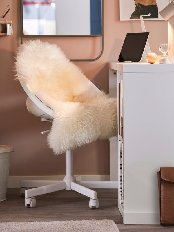 A small home workspace with a white LOBERGET/MALSKÄR swivel chair covered with an ULLERSLEV sheepskin by a white KALLAX desk.