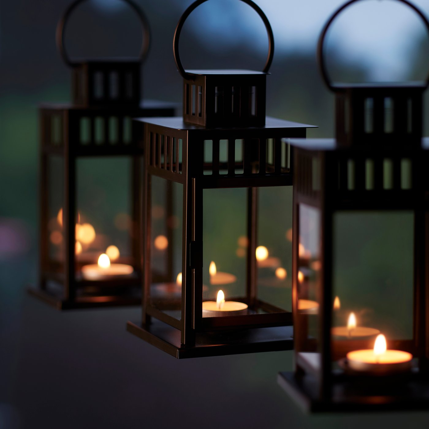Three black BORRBY lanterns placed side by side, each with a lit tealight inside.