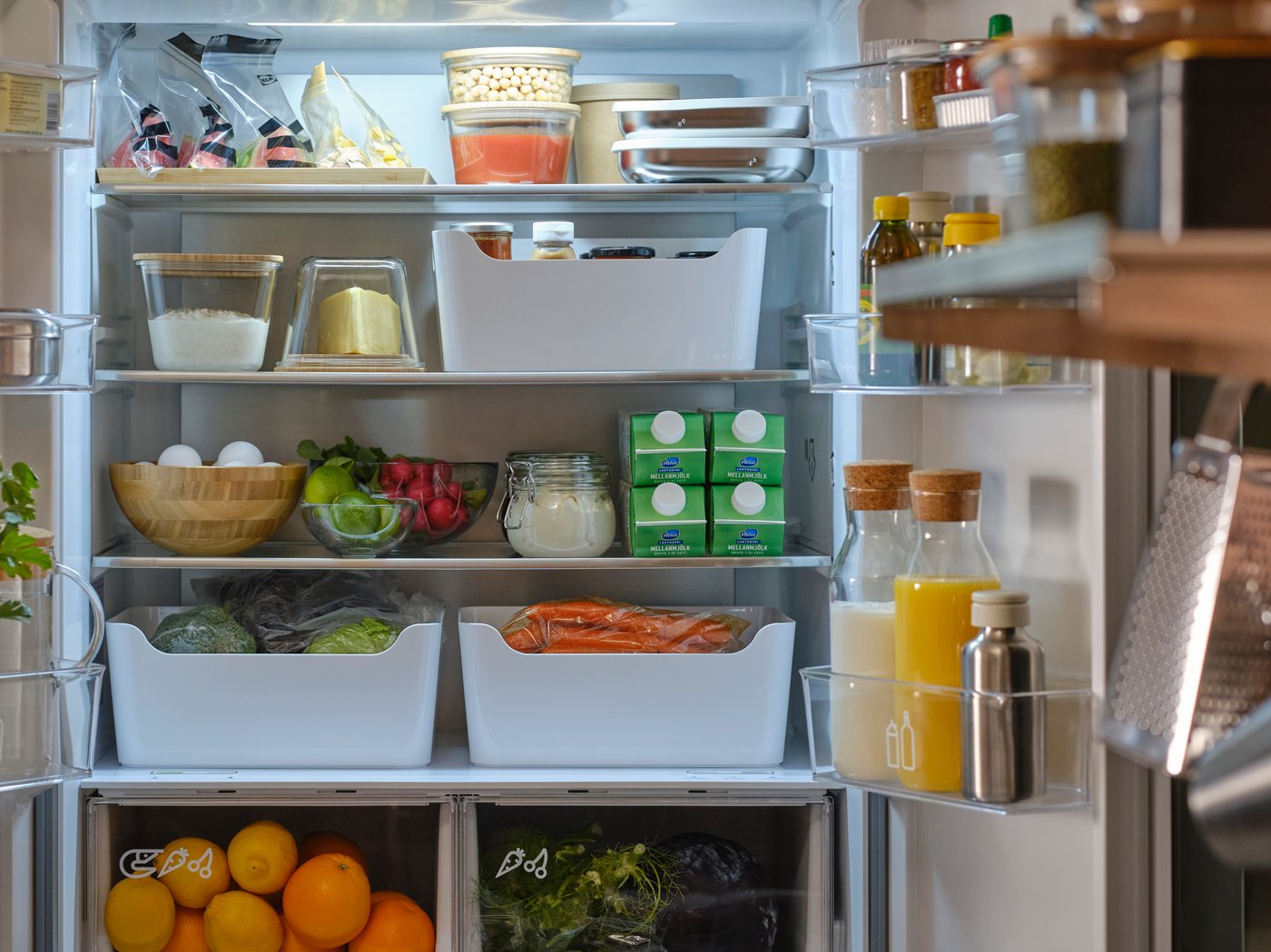 Un refrigerador de puertas francesas con ambas puertas abiertas que muestran alimentos en contenedores, cajas, frascos, bolsas resellables y garrafas.
