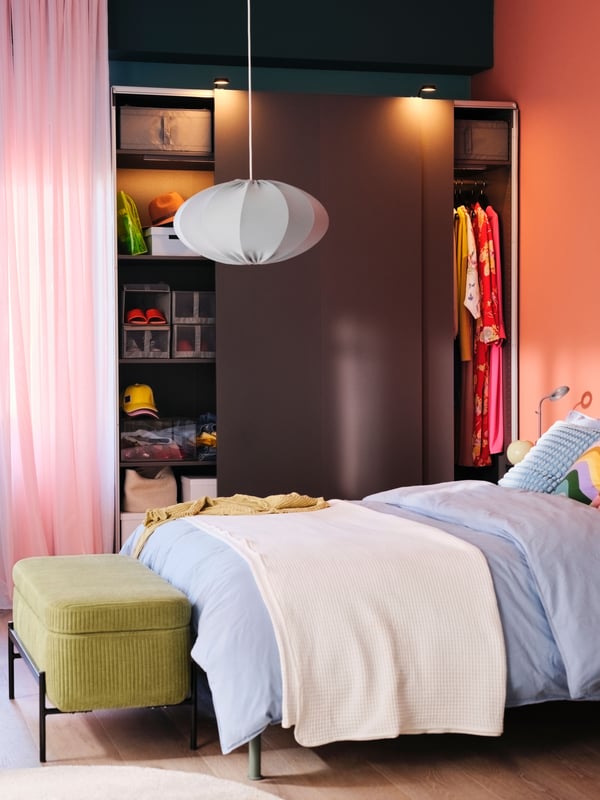 A dark grey PAX/HASVIK wardrobe with the sliding doors open behind a bed covered in a grey-blue ÄNGSLILJA bed linen.