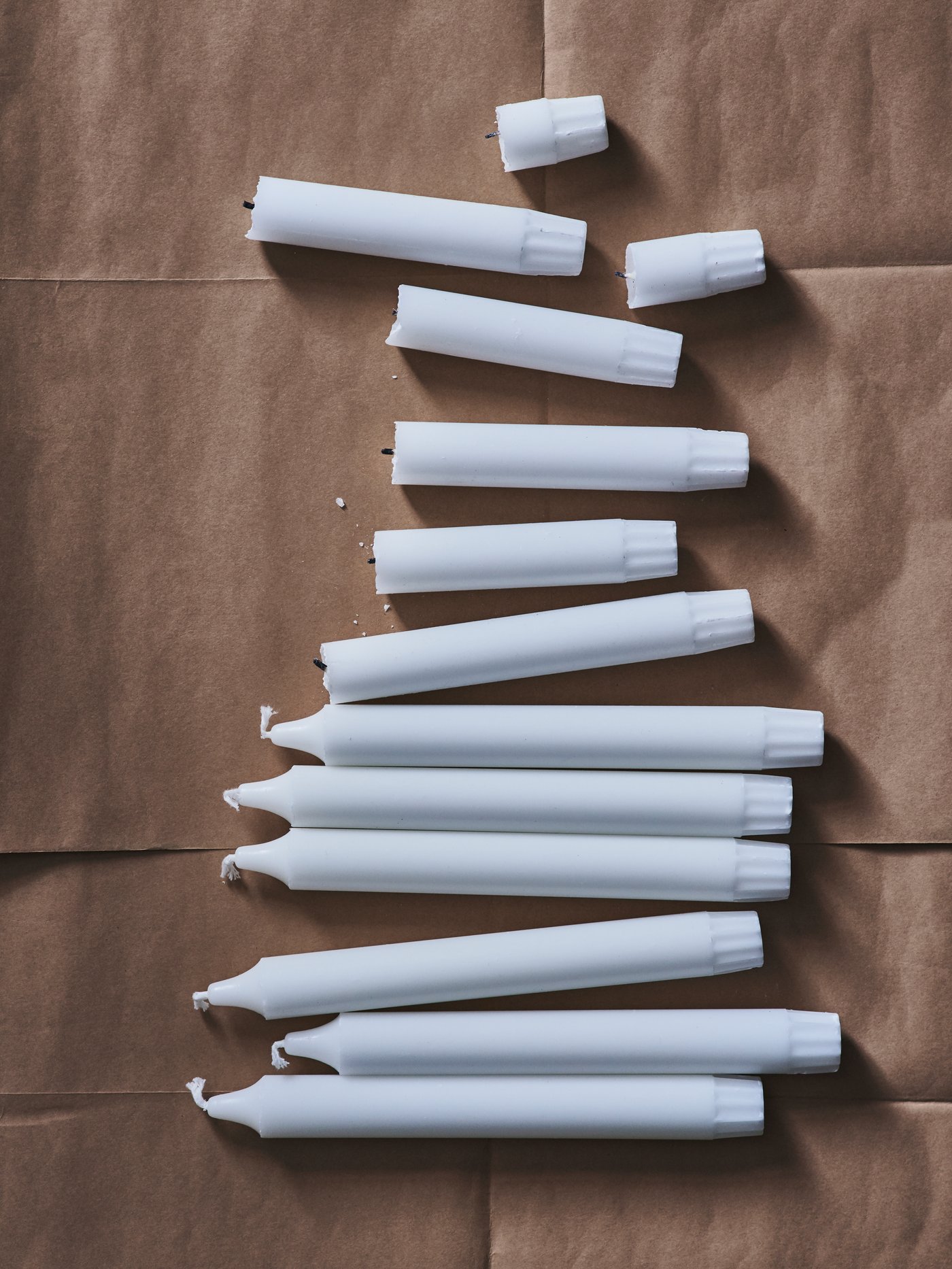 Eine Reihe von JUBLA unparfümierten Kronleuchterkerzen in einer Reihe auf einem Untergrund aus Packpapier.