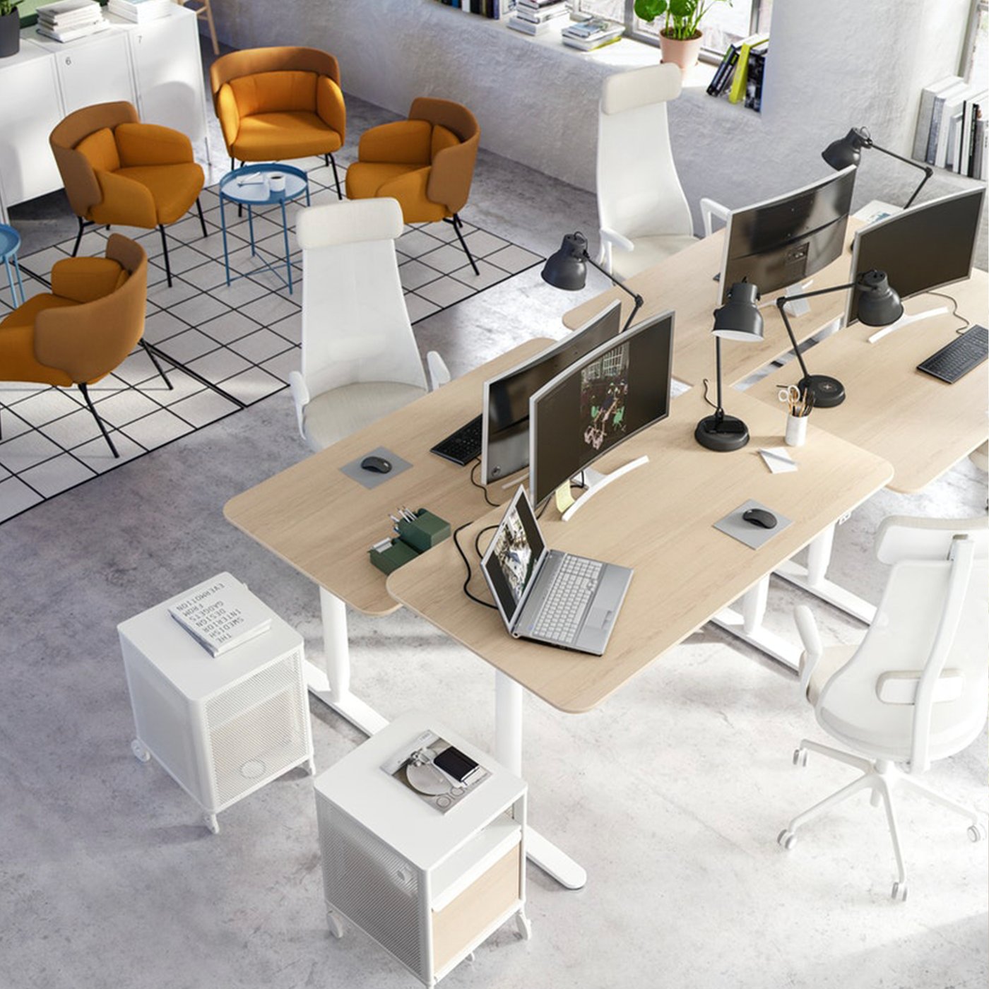 Moderna uredska prostorija s radnim stolovima, računalima, narančastim foteljama i plavim stolićem.