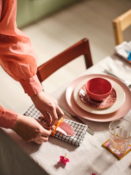 Person at a dining table arranging a folded tea towel made of cotton fabric with geometric print, next to set of dishes.