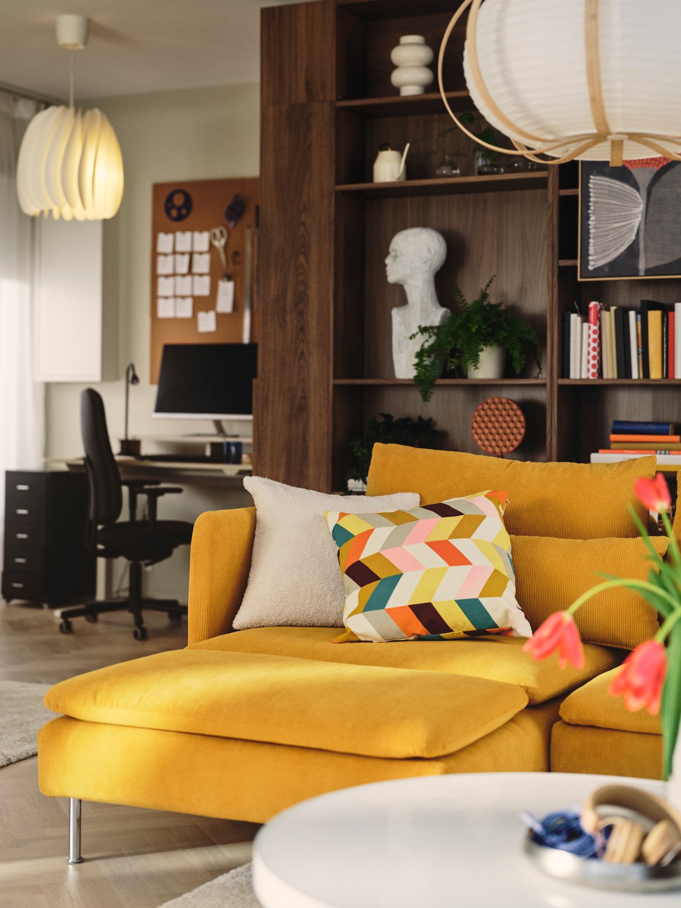 A living room features a dark yellow SÖDERHAMN 4-seat sofa-bed with a chaise longue, surrounded by decorative cushions.