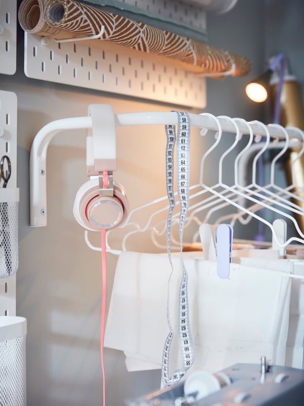 A NÄVLINGE clamp spot lights up garments on STAJLIG hangers on a MULIG clothes bar, wall-mounted next to SKÅDIS pegboards.