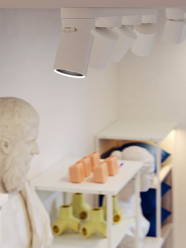 White NYMÅNE ceiling spotlights with 4 spots highlight wall-mounted PLATSA open shelving units displaying home deco objects.