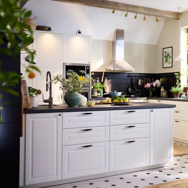 Kuchnia z białymi frontami, na środku znajduje się wyspa z akcesoriami.