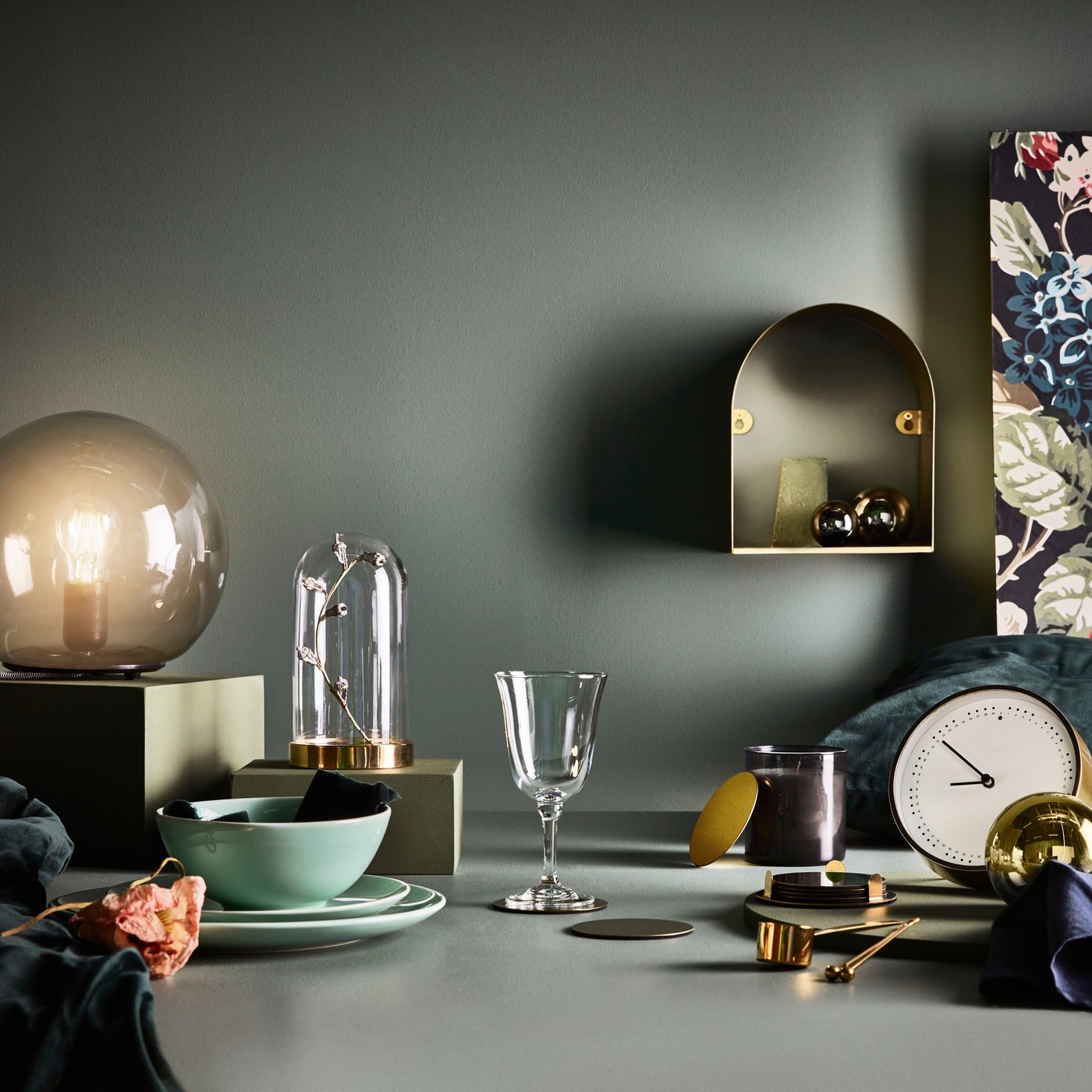 Viele verschiedene Gegenstände und Utensilien vor einem dunklen Hintergrund, u. a. mit einer Uhr, einer Tischleuchte und einer Glasglocke.