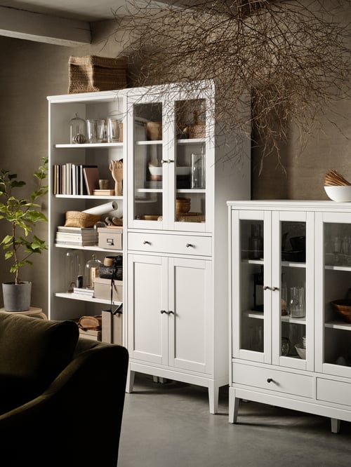 A white bookcase, a white high cabinet with glass doors and 1 drawer, a white cabinet with bi-folded glass doors.