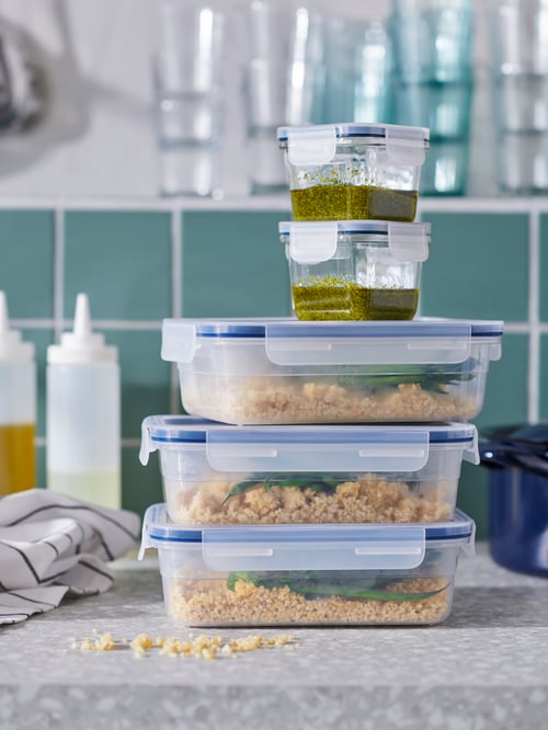 A stack of IKEA 365+ food containers, big and small, filled with food and standing amid kitchen accessories on a worktop.