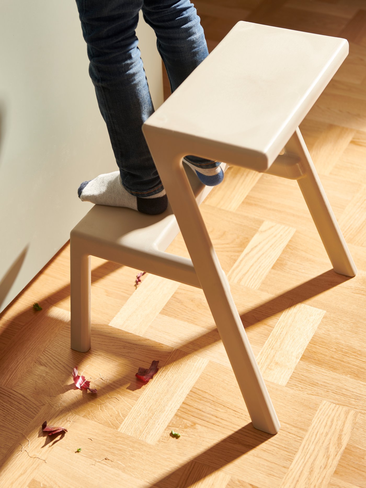 Ein Kind steht auf einem MÄSTERBY Tritthocker, auf dem Boden liegen um den Hocker herum Zwiebelschalen.