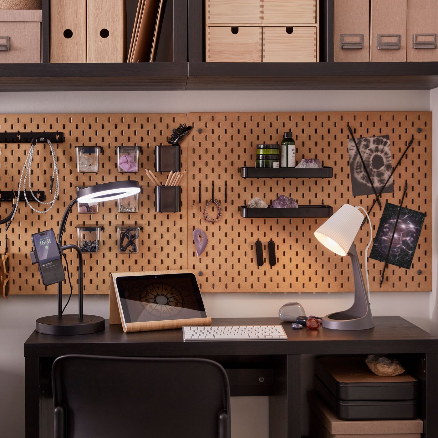 Es ist ein kleiner Arbeitsplatz mit einem schwarzbraunen KALLAX Schreibtisch mit Arbeitsleuchten und Regalen und SKÅDIS Lochplatten an der Wand zu sehen.