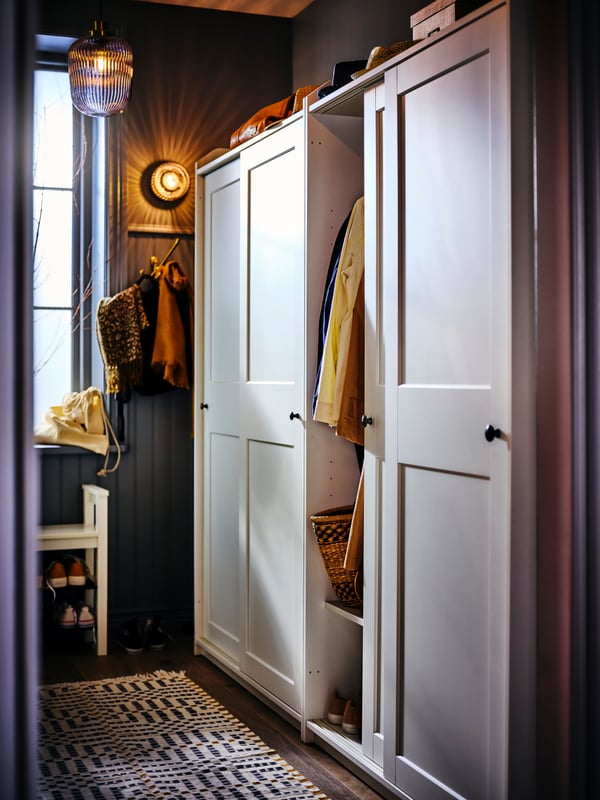 Un clóset IKEA blanco con puertas corredizas. Una de ellas abierta mostrando la ropa en el interior.