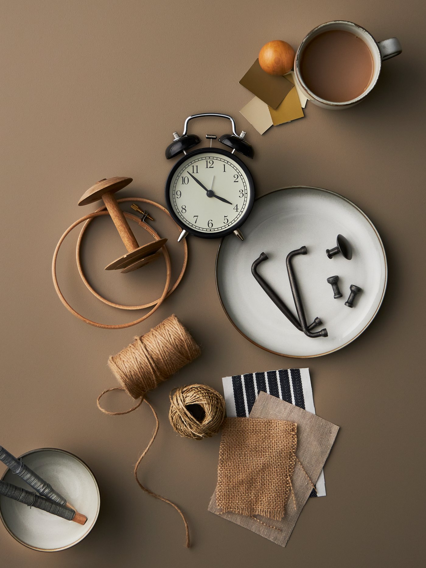 Un reloj despertador DEKAD negro y piezas de la vajilla GLADELIG dispersas con retazos de tela y cuerda de color natural.