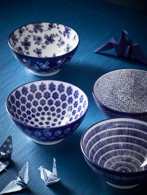 Großaufnahme des blauen Esstisches mit vier Servierschüsseln in Weiß und Blau. Darum verteilt stehen gefaltete Origami-Kraniche.