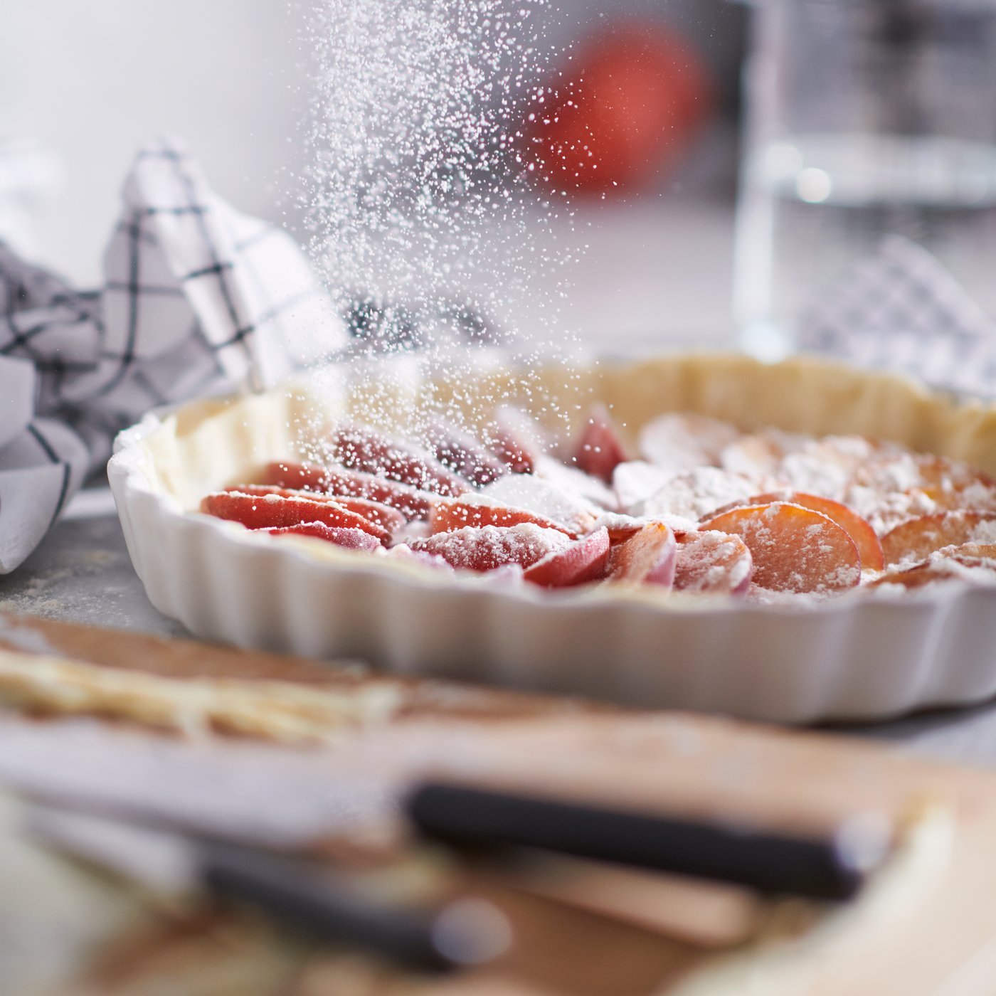 En tærte bagt i et råhvidt VARDAGEN tærtefad bliver drysset med flormelis i et køkken