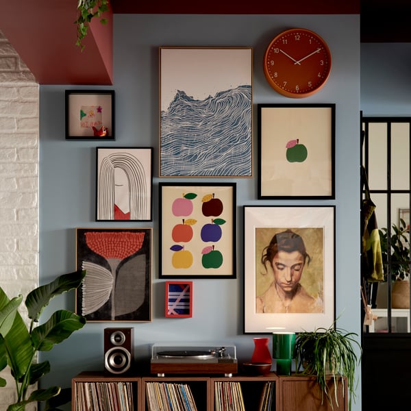 A living room wall adorned with various colourful artworks, featuring BLODFLÄDER pictures in blue, red, and green hues.