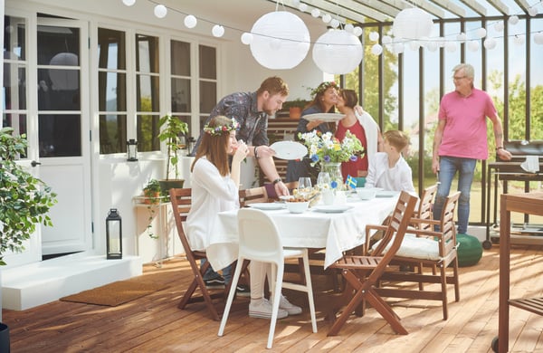 Veranda con gente attorno a una tavola decorata con fiori, bandierine della Svezia e lampade a sospensione appese sopra.