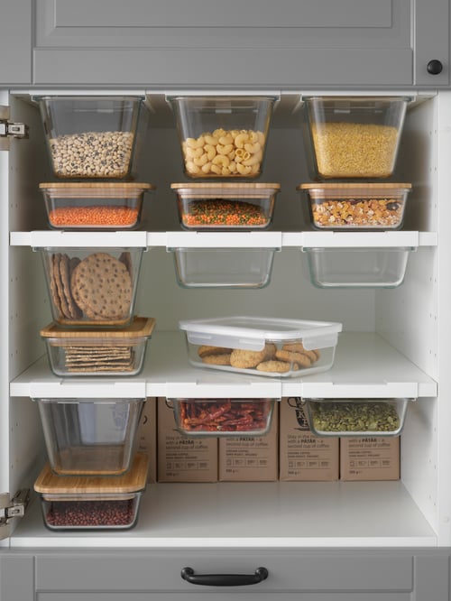 O secțiune deschisă a unui dulap care conține mai multe recipiente pentru alimente cu capac cu produse alimentare, unele în suporturi pentru recipiente.