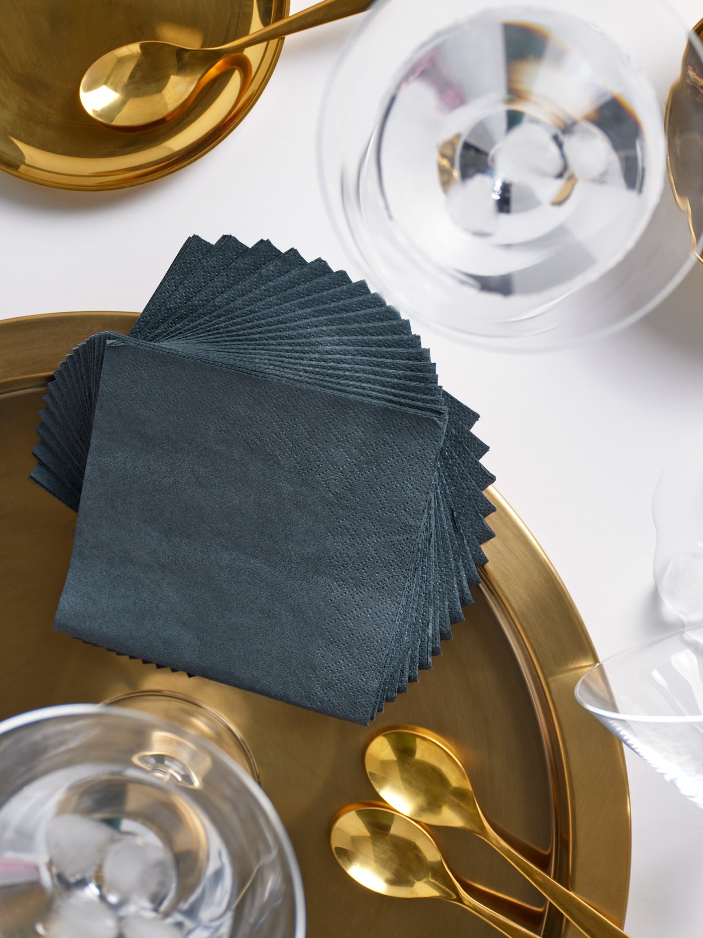Man sieht einen gedeckten Tisch in weiß-gold und auf einem goldenen Teller liegen mehrere FANTASTISK Papierservietten in dunkelgrau