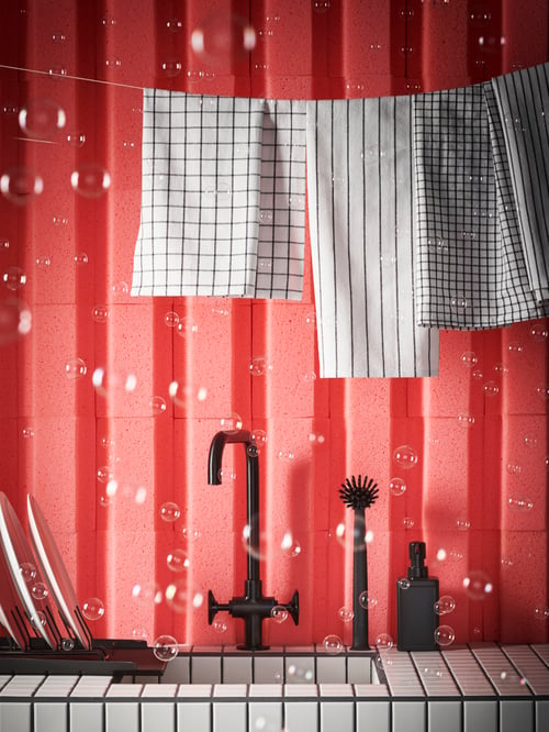 Black RINNIG drainer, brush and dispenser at tile sink with black tap, hanging tea towels and pink sponge wall with bubbles.