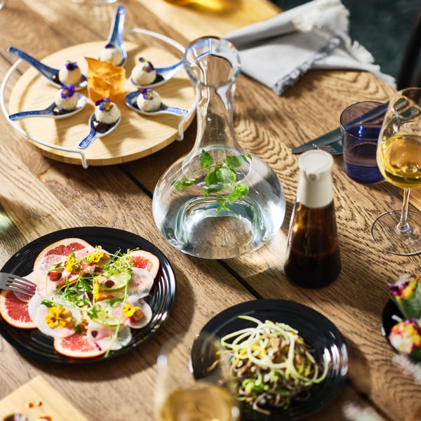 A MÖRBYLÅNGA table in dark oak veneer is set with different coloured plates and festive dishes and a STORSINT carafe.