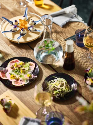 A MÖRBYLÅNGA table in dark oak veneer is set with different coloured plates and festive dishes and a STORSINT carafe.