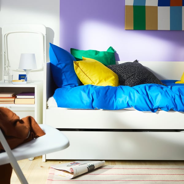 VIHALS day-bed in white, with trundle bed below and the wall behind it painted purple. Bright blue and yellow bedding.